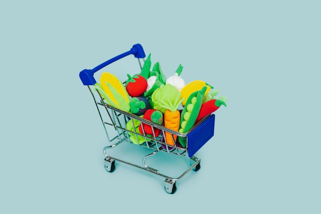 Different plasticine vegetables in a shopping cart on a blue background