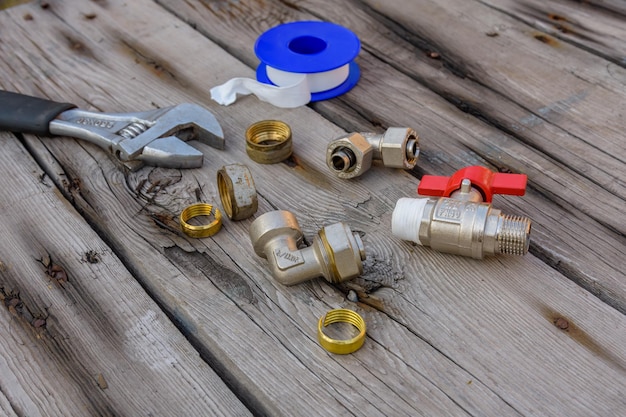 Different plumbing spare parts sealing tape and adjustable wrench on a wooden background