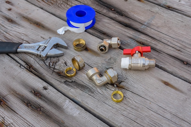 Different plumbing spare parts, sealing tape and adjustable wrench on a wooden background