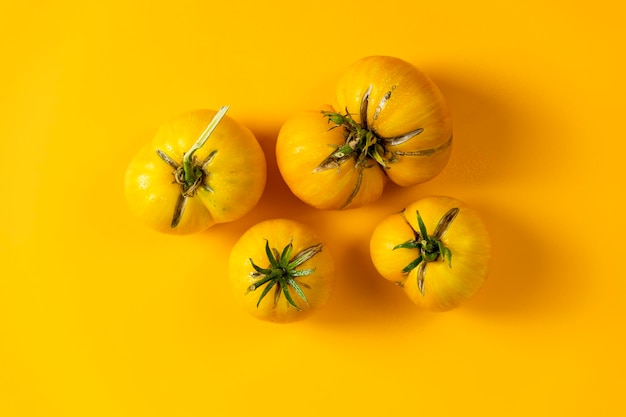 Different raw fresh yellow tomatoes on yellow background