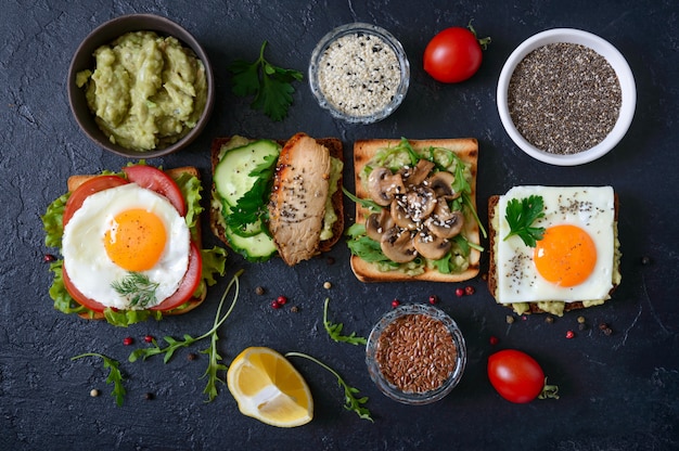 Different sandwiches on a black table. Tasty healthy appetizer with avocado. Quick breakfasts. Healthy eating concept. Proper nutrition. Top view.