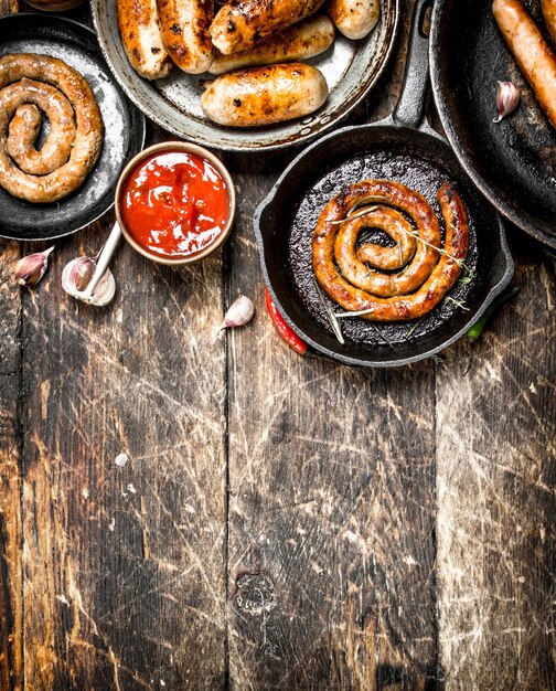 Different sausages in pans with tomato sauce on a wooden background