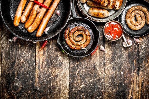 Different sausages in pans with tomato sauce on a wooden background