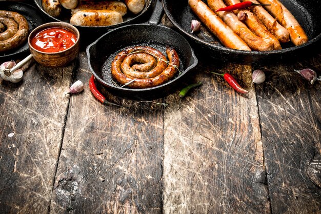 Different sausages in pans with tomato sauce on a wooden background