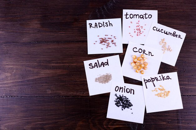 Different seeds on pieces of paper on wooden background