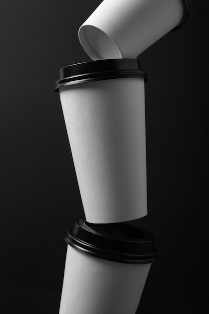 Different size white paper coffee cups with black lid on black background