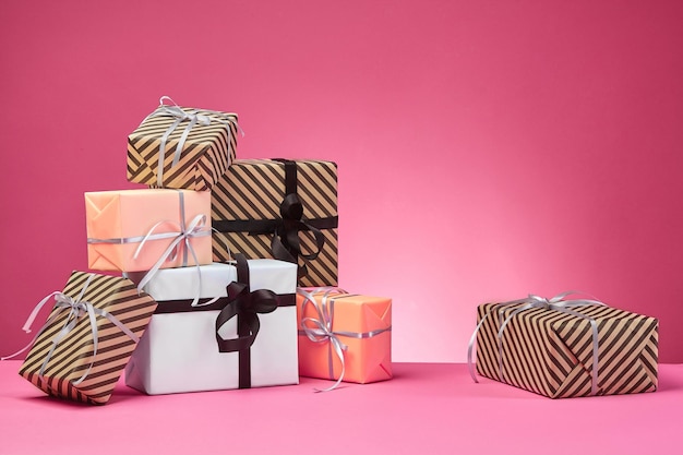 Different sizes colorful striped and plain paper gift boxes tied with ribbons and bows on a pink sur