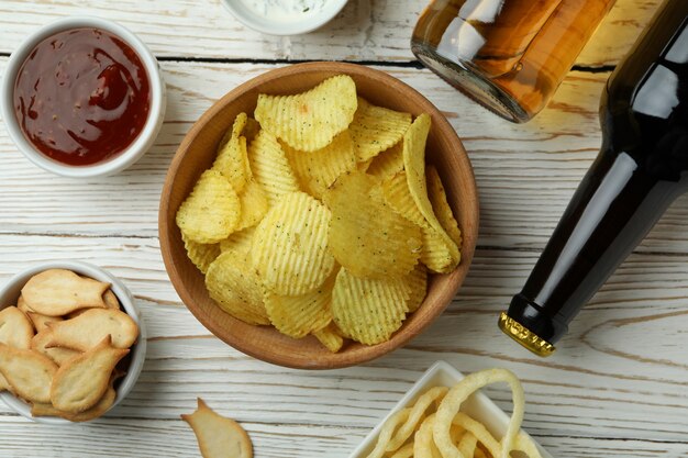 Different snacks, beer and sauces on white wooden surface