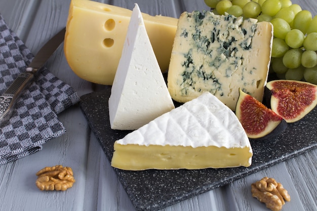 Different sorts of cheese and fruits on the grey cutting board