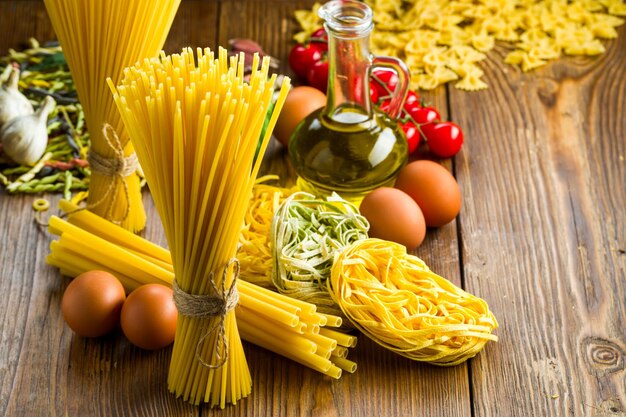 Different sorts of raw pasta next to egg in flour