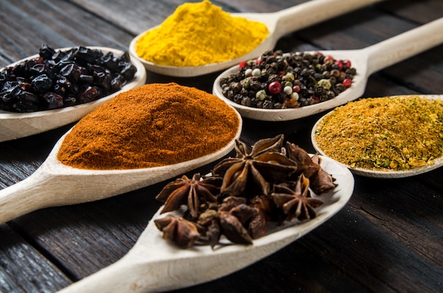 Different spices in wooden spoons on a black wooden table