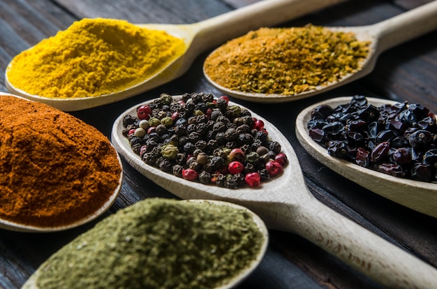 Different spices in wooden spoons on a black wooden table