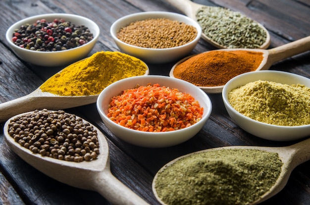 Different spices in wooden spoons on a black wooden table