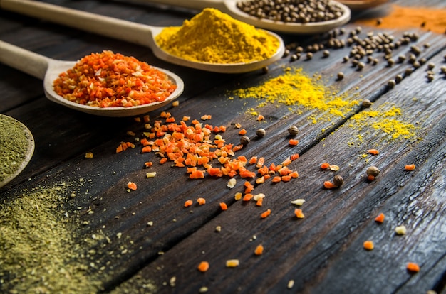 Different spices in wooden spoons on a black wooden table