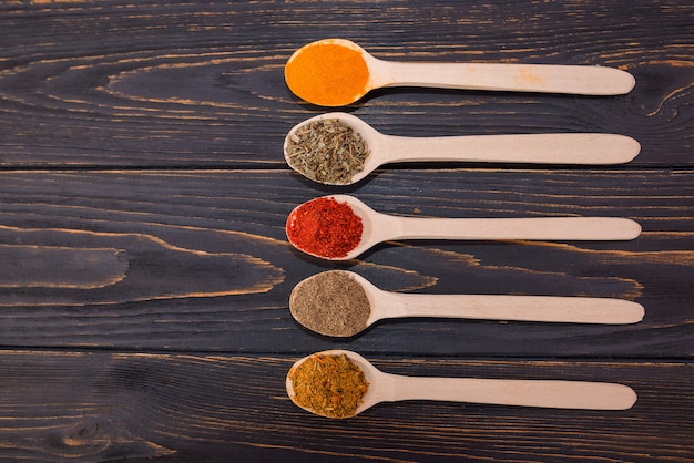 Different spices in wooden spoons on a wooden background.