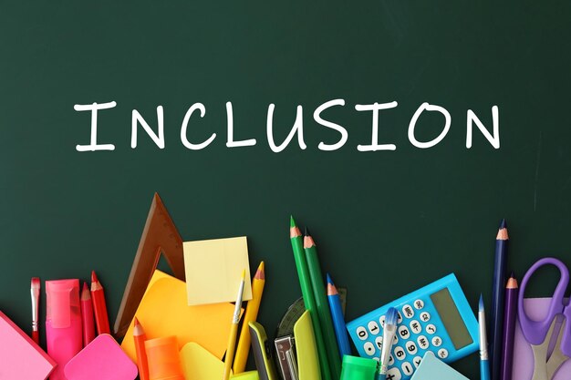 Different stationery on green chalkboard and word INCLUSION flat lay