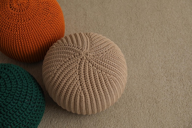 Different stylish knitted poufs on carpet indoors space for text