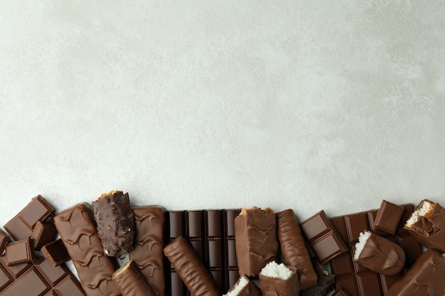 Different tasty candy bars on white textured background