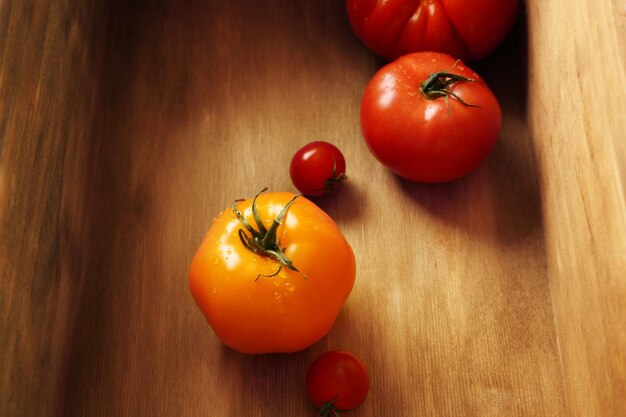 Different tomatoes with water drops in wooden box