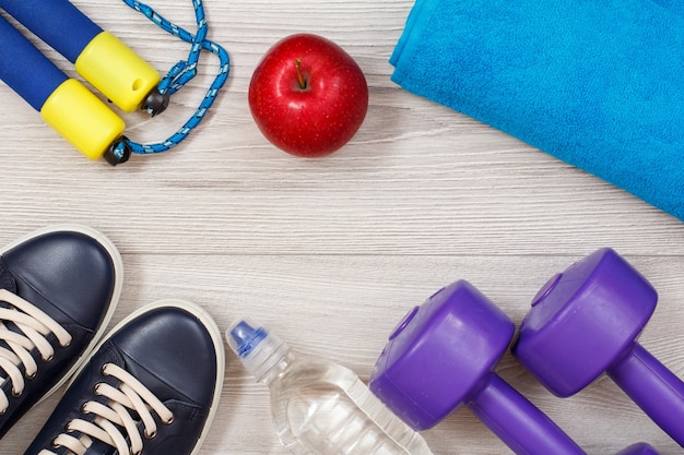 Different tools for fitness with bottle of water and apple in room or gym on gray floor.