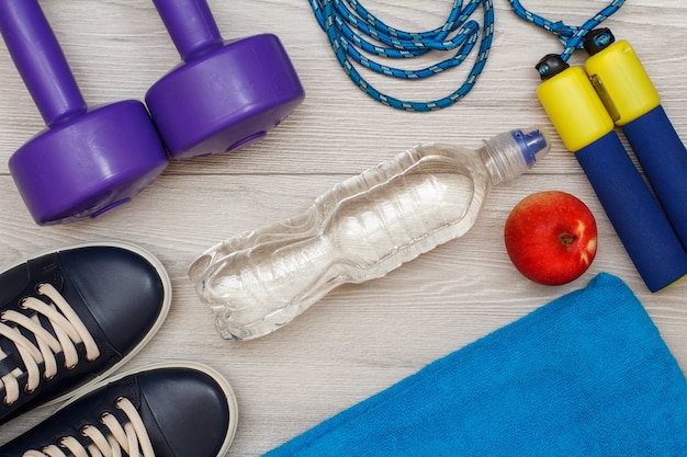 Different tools for fitness with bottle of water and apple in room or gym on grey floor