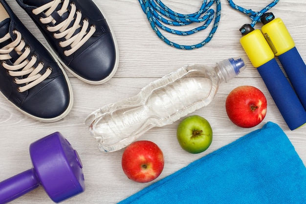 Different tools for fitness with bottle of water and apples in room or gym on grey floor