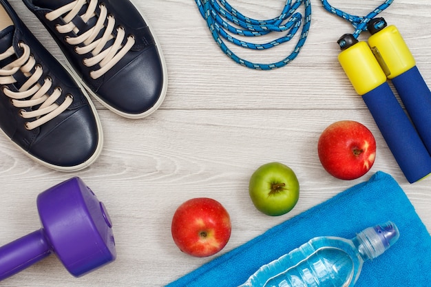 Different tools for fitness with bottle of water and apples in room or gym on grey floor