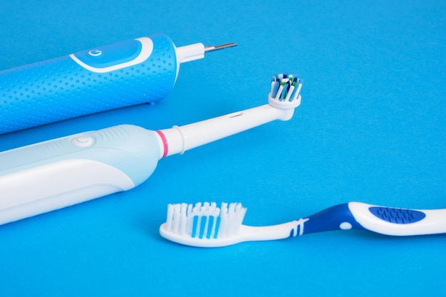 Different toothbrushes on blue background electric toothbrush\
or plastic toothbrushes ecofriendliness lifestyle concept\
efficiency of brushing teeth