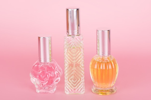 Different transparent perfume bottles on pink background