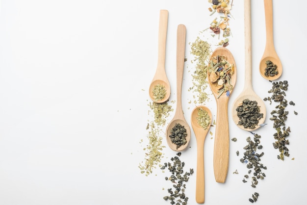 Different type of herbs on wooden spoon against white backdrop