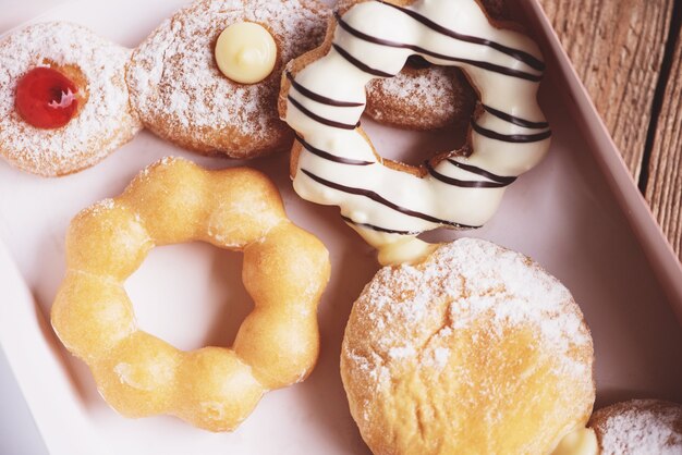 Фото Различные типы набора пончиков, сладкие пончики в бумажной коробке с пончиками, десертные закуски.