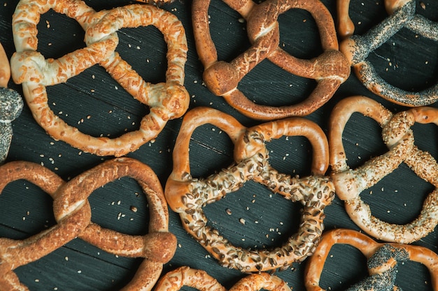 Diversi tipi di pretzel al forno o bagel con semi su sfondo nero