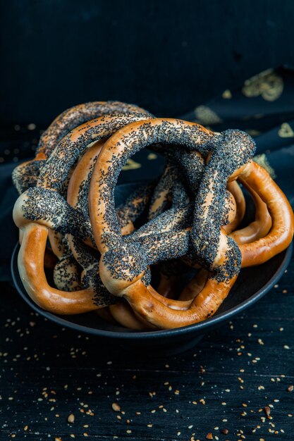 黒の背景に種が付いた焼きたてのプレッツェルまたはベーグルのさまざまな種類