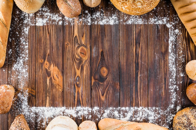 Different types of bread spread at the edge of flour on wooden table