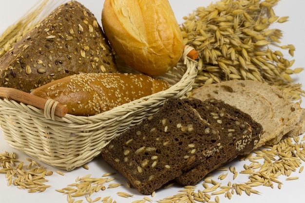 Diversi tipi di pane: bianco e nero con semi, baguette e panini in un cesto di vimini. chicchi di avena e rametti di avena