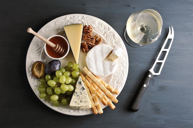 Different types of cheese with mildew, grapes honey and nuts on a plate, a glass of wine