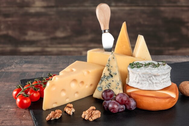 素朴な木製の背景に黒いスレートボードにクルミとブドウとさまざまな種類のチーズ