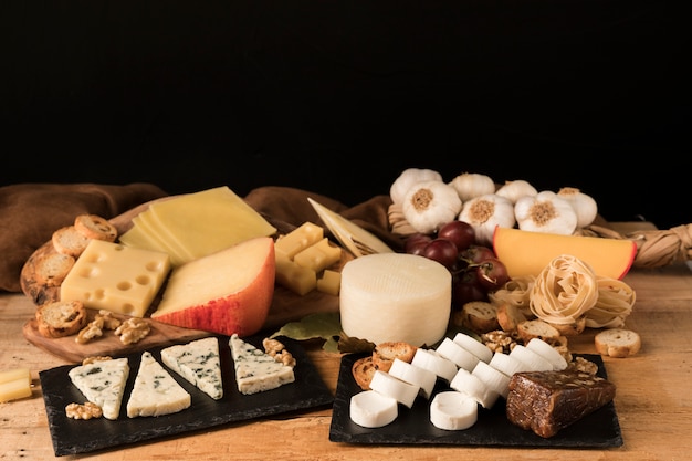Различные виды сыров располагаются в сланцевом камне в деревянном столе.