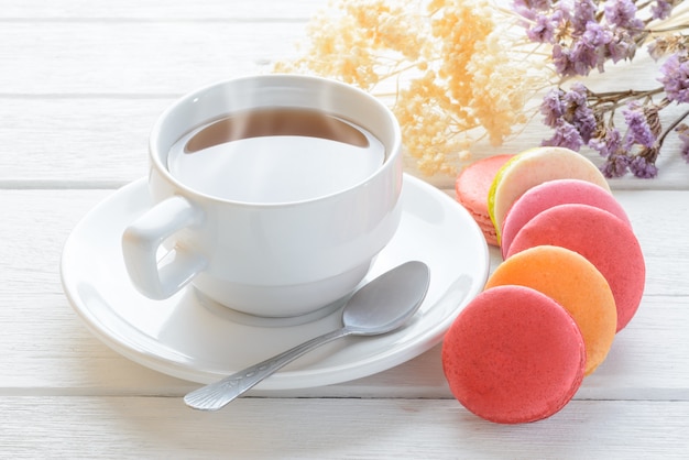 Different types color of macaroons with Cup of hot tea on white wooden background