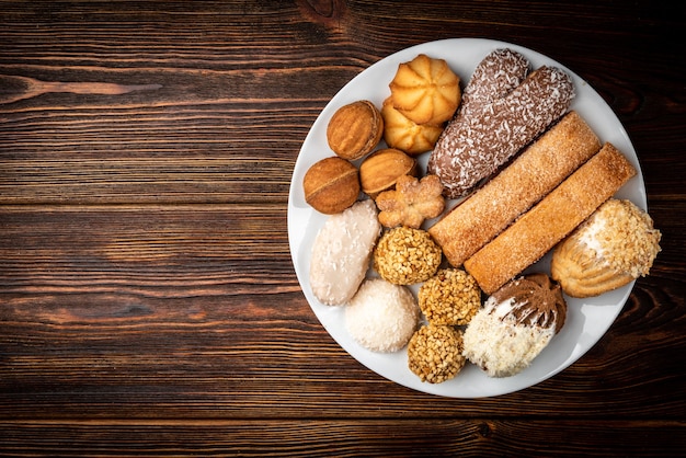 Different types of cookies on white plate on dark wooden background.