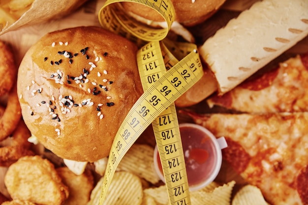 Photo different types of fast food and snacks on table with measuring tape