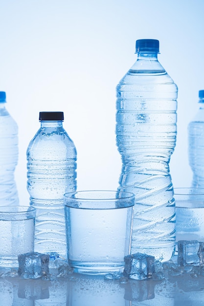 Different types of ice mineral water bottle with glasses of\
water on blue background vertical format