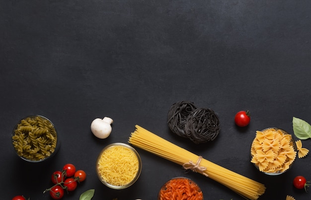 Different types of Italian pasta with vegetables on the dark chalkboard