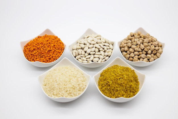 Different types of legumes in small bowls on a white background