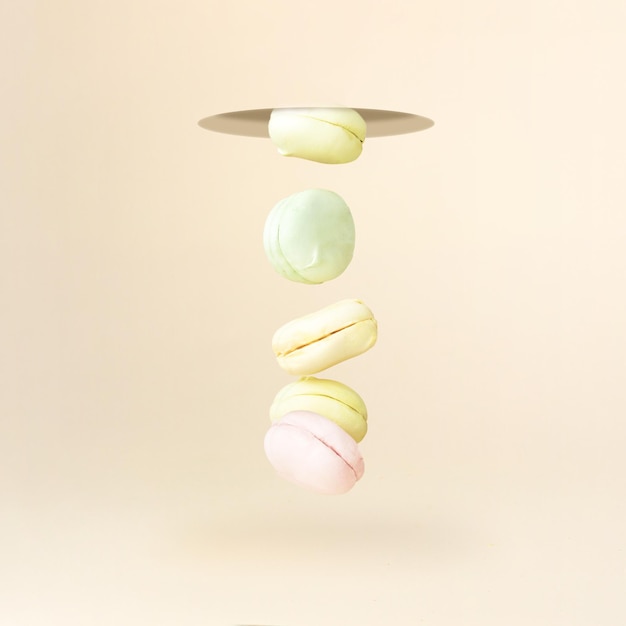 Different types of macaroons marshmallow in motion falling down on pastel coral background oncept of sweet dessert