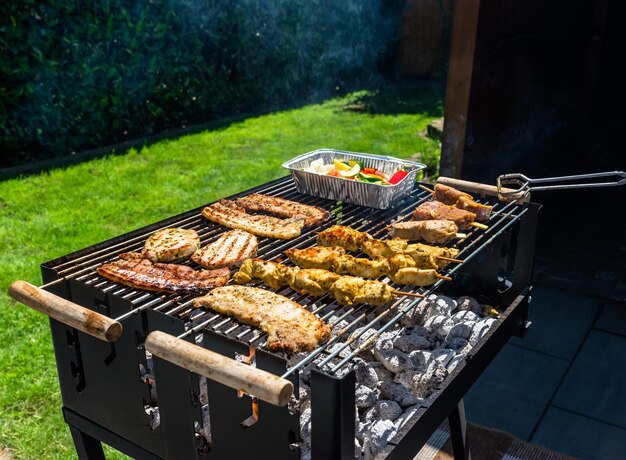 Photo different types of meat fried on the home grill standing on a home garden on the paving stone