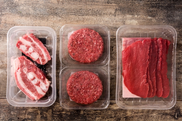 Different types of meat packaged in plastic on wooden table