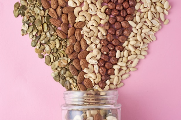 Different types of nuts and seeds in a glass jar on pink background