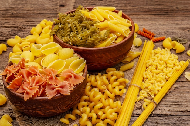 Разные виды макарон в керамических мисках. Традиционная итальянская еда, концепция здорового питания. Деревенский деревянный стол