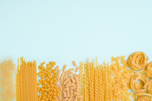 Different types of pasta from wheat varieties laid out in a line on a light wine background